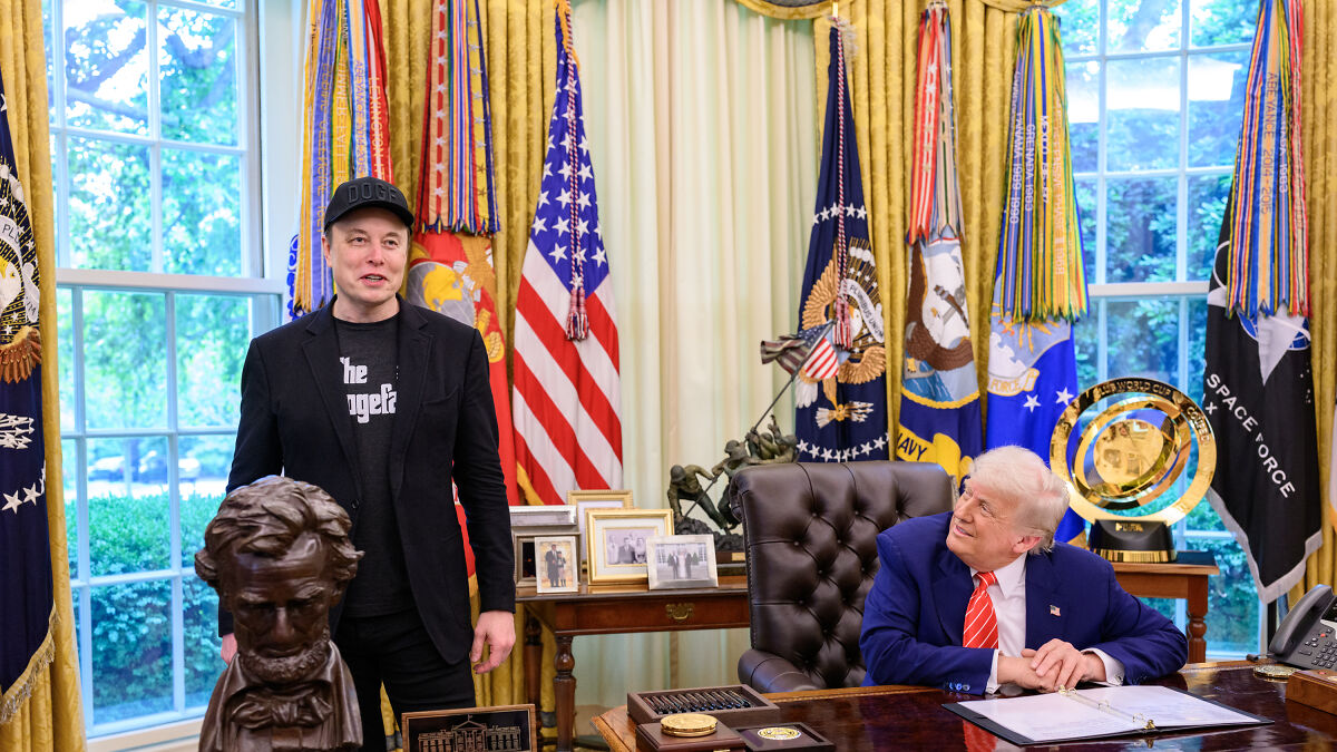 Elon Musk and Donald Trump in the Oval Office with flags and presidential decor during a formal meeting.