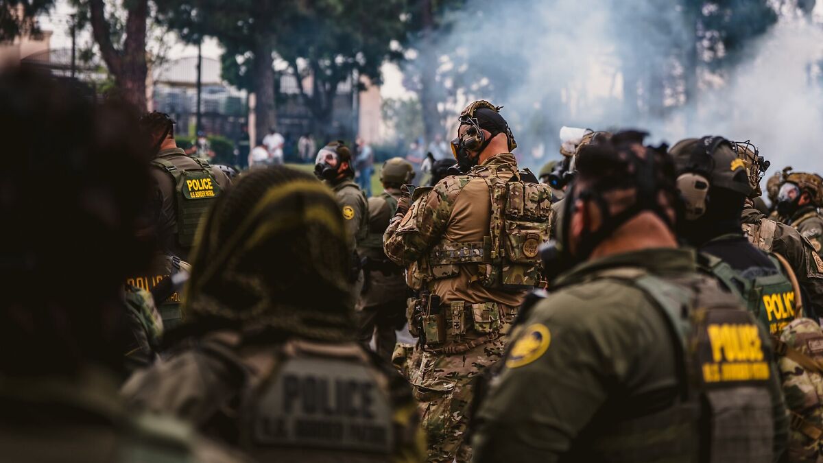 Heavily armed cops in tactical gear at a riot scene with smoke, preparing during LA unrest and National Guard deployment.