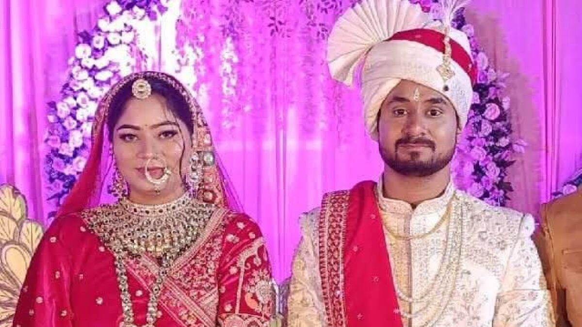Bride and groom in traditional Indian wedding attire posing in front of floral decorations on their wedding day.