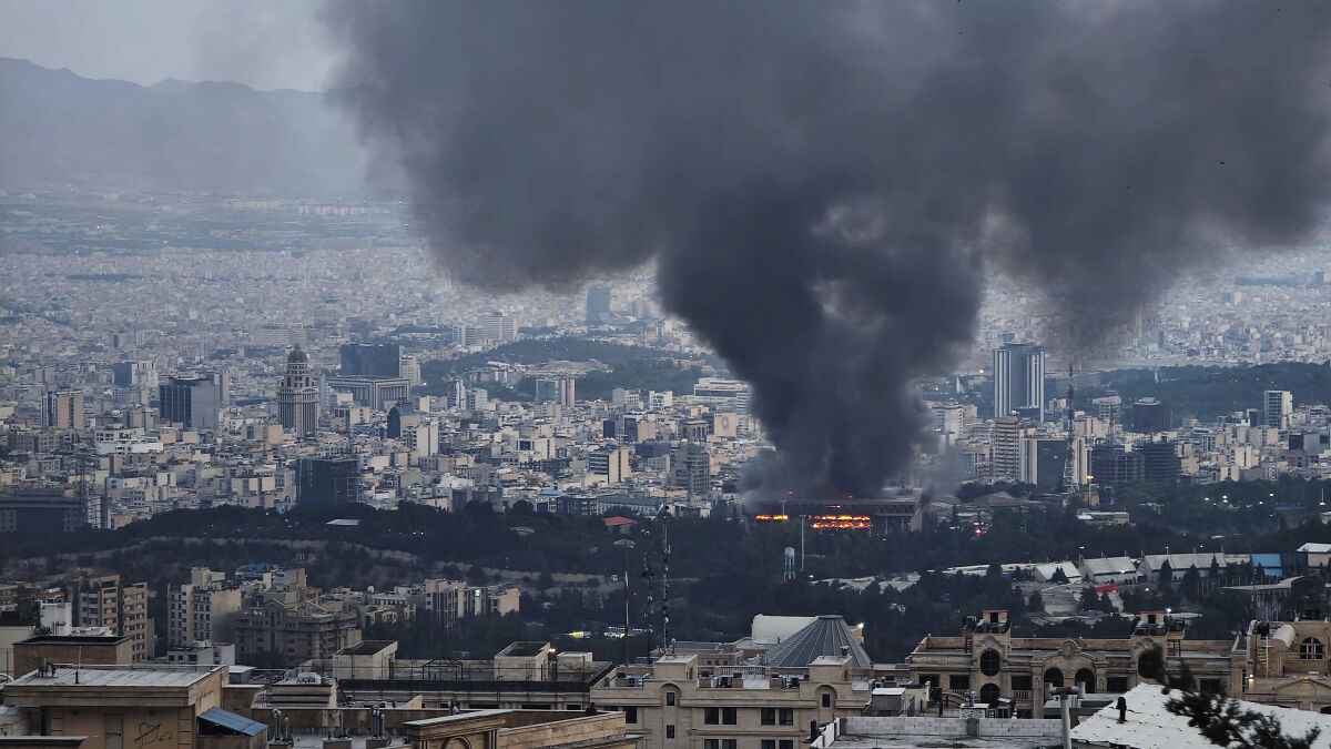 Thick black smoke rises over a city after an Israeli missile strike on Iran state TV building.