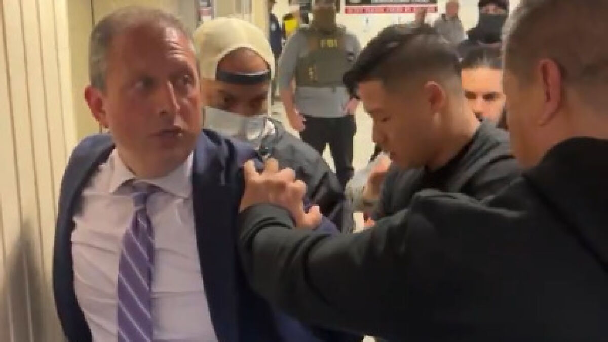 Brad Lander, running for New York mayor, being detained by ICE agents in a crowded indoor hallway.