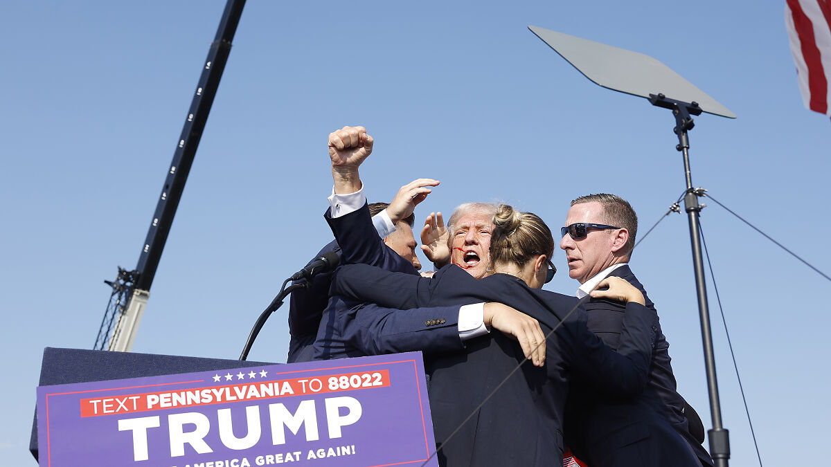Trump surrounded by security personnel during a public event amid an assassination attempt footage release.