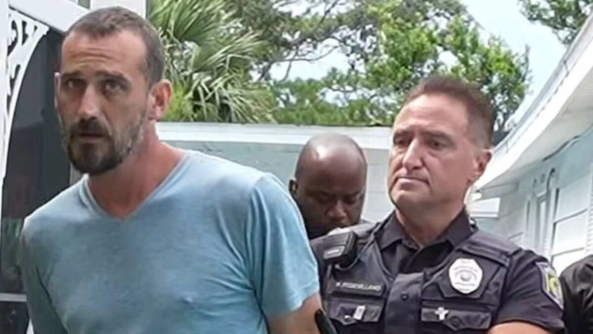 Man in blue shirt being escorted by police officers outside a building in Florida related to baby boy death case.