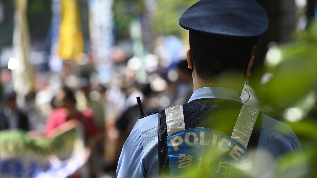 Police officer in uniform monitoring a crowded street in Japan amid Twitter killer case developments.