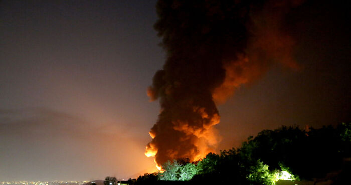 Nighttime scene with blazing rockets creating fire and smoke near a calm crowd on rooftops in Israel.
