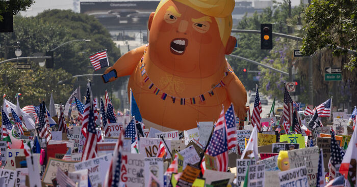 Protesters at No Kings Rally with an inflatable balloon and numerous American flags visible during the demonstration.