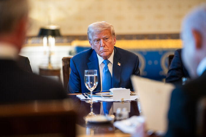 Former President Trump seated at a table during a meeting, with focus on a Trump senior advisor discussing Epstein client list.