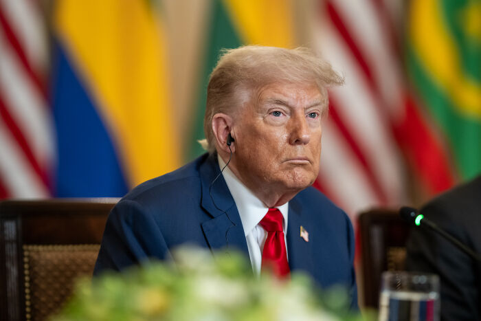 Former president in a blue suit with a red tie seated at a conference with flags blurred in the background, DOJ subpoenas doctors keyword.