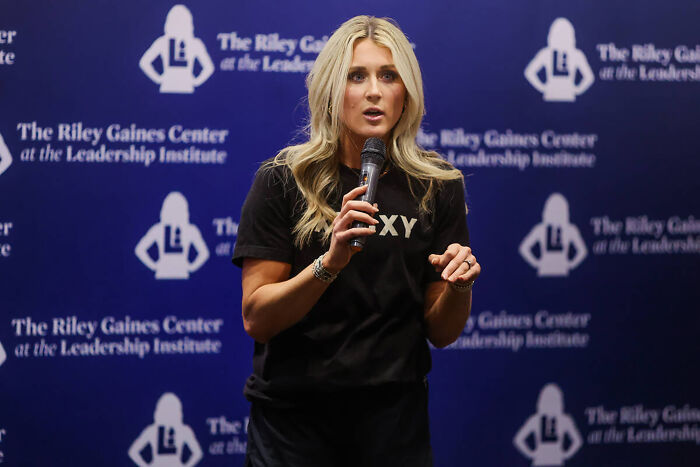 Speaker at The Riley Gaines Center holding a microphone, discussing topics related to trans swimmer Lia Thomas records removal.