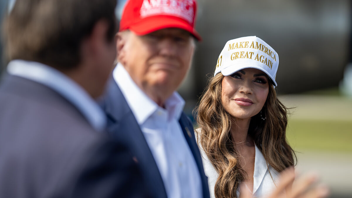 Donald Trump and Kristi Noem wearing Make America Great Again hats at an outdoor political event discussing ICE flight story.