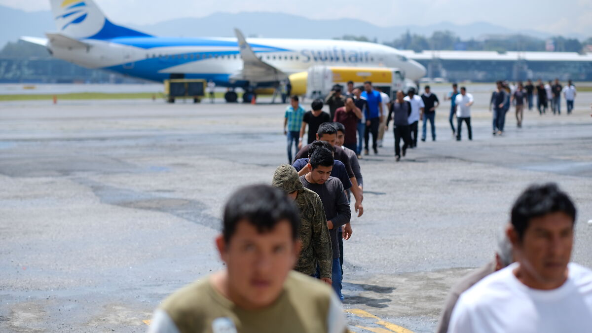 A line of people walking at an airport tarmac near a parked airplane, illustrating deportation of American citizens.