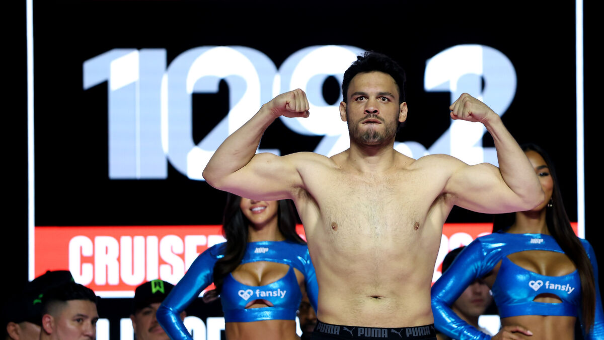 Boxing champion flexing muscles during weigh-in, with promotional models and digital timer in the background.