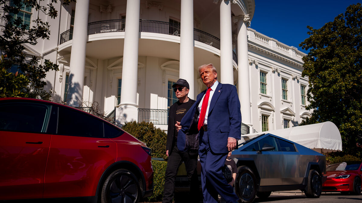 Former President Trump and Elon Musk walking outside the White House near electric vehicles discussing disruption in U.S. politics.