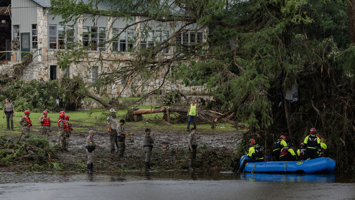 Rescue team in life jackets conducting Texas flood search and rescue operation near muddy riverbank.