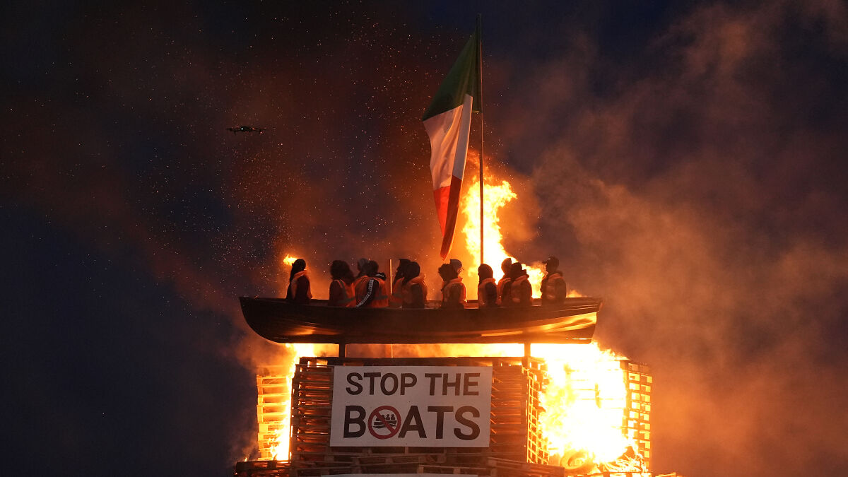 Bonfire with mock migrant boat and life jackets set alight at night sparking outrage over racist display.