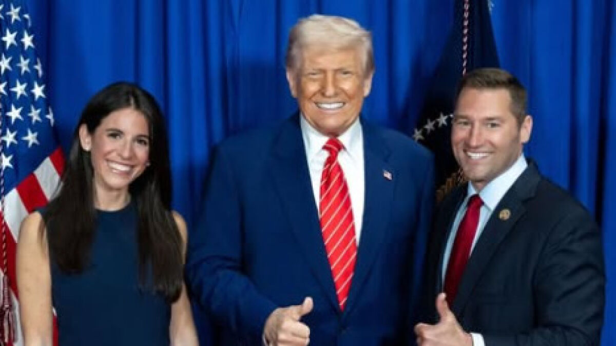 Republican lawmaker and Fox News journalist posing together, smiling with American flags and blue curtains behind them.